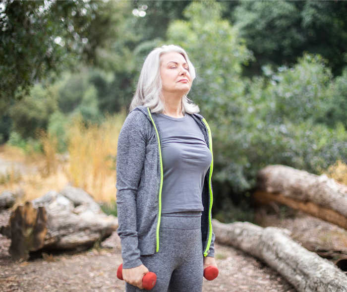 Leben mit NET: Eine ältere Frau mit Hanteln im Wald