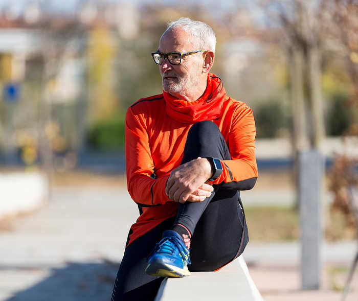 Leben mit NET: Ein älterer Patient ruht sich nach einer Sporteinheit auf einer Mauer sitzend aus Leben mit NET: Ein älterer Patient ruht sich nach einer Sporteinheit auf einer Mauer sitzend aus