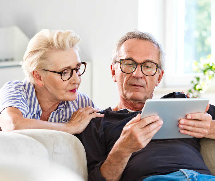 Ein älteres Paar schaut gemeinsam auf ein Tablet, das der Mann in den Händen hält.