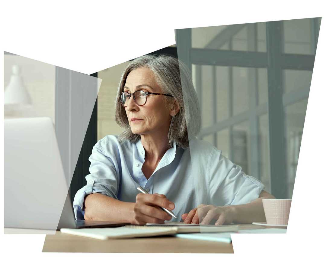 Grauhaarige Frau notiert sich etwas von ihrem Laptop Grauhaarige Frau notiert sich etwas von ihrem Laptop