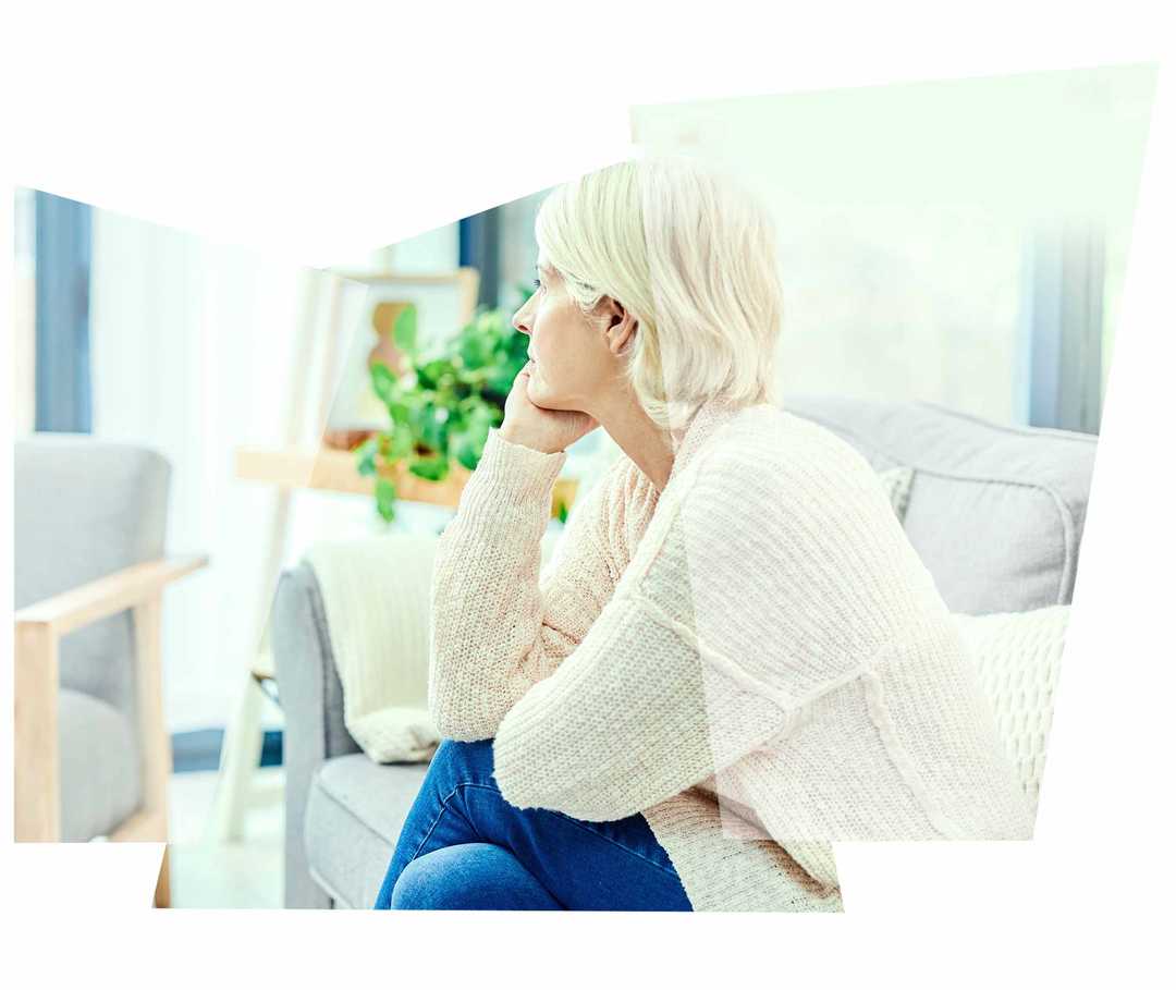 Eine blonde Frau sitzt auf dem Sofa und schaut in Gedanken zum Fenster