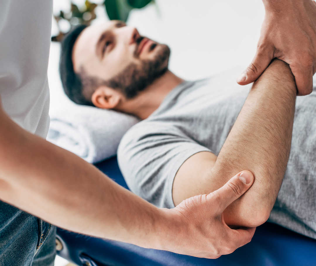 Leben mit NET: Ein Pysiotherapeut behandelt den Ellenbogen eines Aptienten